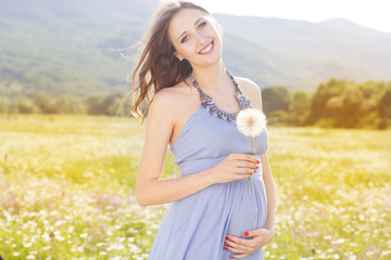 Fototapeta na wymiar Pregnant woman with dandelion in hands
