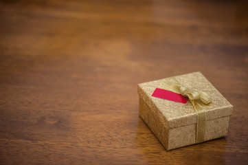 Golden gift box with bow and a small card on a wooden table