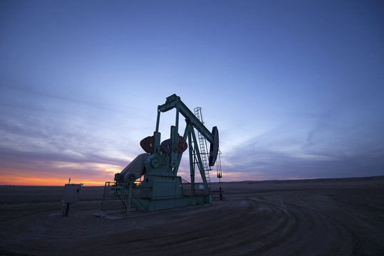 A pumpjack at an oil drilling site at sunset.