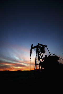 A pumpjack at an oil drilling site at sunset.