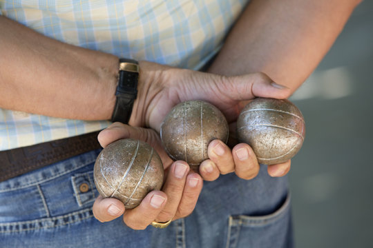 Boules player holding three metal boules behind back