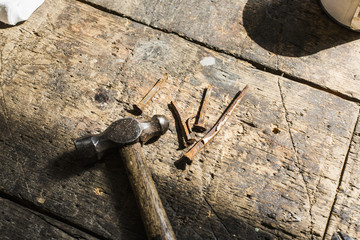 A workbench used by a carpenter or restorer. Worn edges, cut saw marks and holes and small rusty nails and a hammer. 