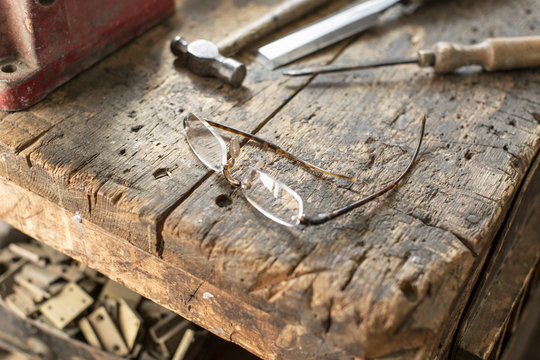 Antique furniture restorer's  workbench. A worn marked block of wood with smoothed edges, a hammer and chisel, and spectacles. 