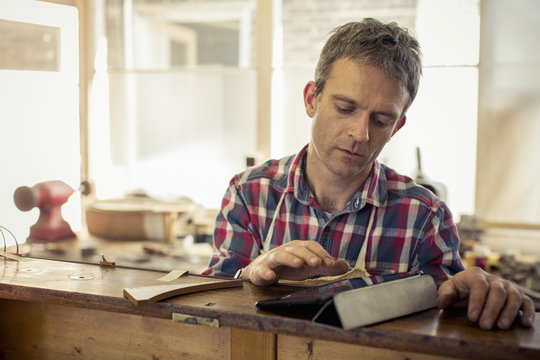 An antique furniture restorer, a craftsman using a digital tablet in the course of his work. 
