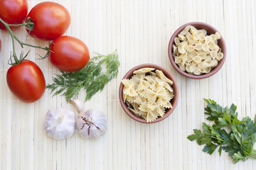 Pasta in a clay pot, tomatoes, herbs and spices on light makisu