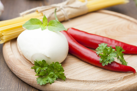 Mozzarella with herbs, noodles, chilli, on a wooden round board, selective focus