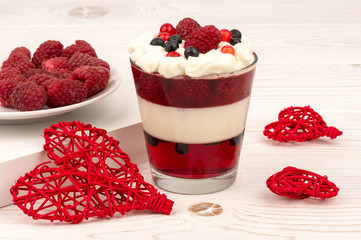 Sweet dessert in glass with cream, jell, raspberries and blueberries on wooden background.