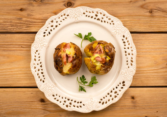 Baked potato with ham and cheese on the plate on the wooden background,
