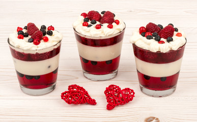 Sweet dessert in glass with cream, jell, raspberries and blueberries on wooden background.