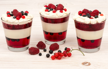 Sweet dessert in glass with cream, jell, raspberries and blueberries on wooden background.