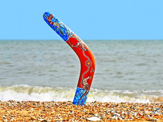 Colorful boomerang on sandy beach against of sea surf. - obrazy, fototapety, plakaty