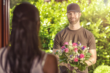 Bearded 20s man delivers flowers to young woman
