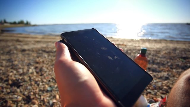 man's hands uses mobile smartphone near the sea at sunset beach