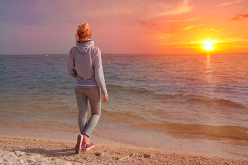 Girl stands with his back to the sea at sunset. Travel to Europe