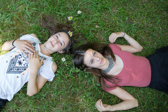 Relaxed young persons (teenage girls) lying in grass and flowers with stretched hand - closed eyes