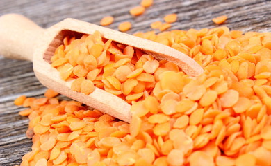 Heap of red lentil with spoon on wooden background