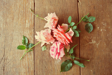 Four pink roses on the rustic wooden table, shot from above. Image filtered in faded, washed out, retro style; nostalgic, romantic vintage concept.