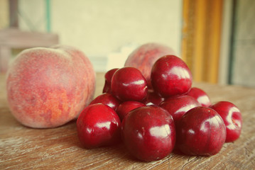 Pile of ripe red fresh cherries and peaches on rustic wooden table, on the terrace of a house. Image edited in faded, washed out, nostalgic, retro style, with Instagram-style red filter.