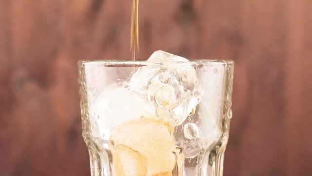 pouring fresh coke with ice cubes isolated on wood background