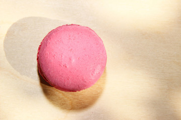 Traditional french pink macaron with sun shadows on wooden background