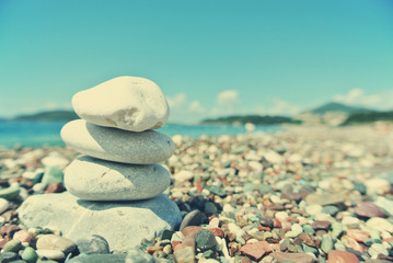 Fototapeta na wymiar Stack of white stones balancing on the pebbly beach, on a sunny day. Image filtered in faded, washed out, retro style; summer vintage concept. Concept of harmony, well-being, wellness and zen.