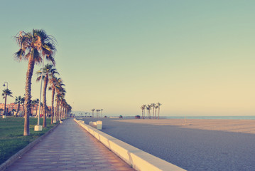 Long sandy beach with palm-lined promenade at sunset. Filtered image in faded, washed-out, retro...