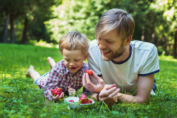 Young father and his son eating strawberries in Park. Picnic. Outdoor portrait