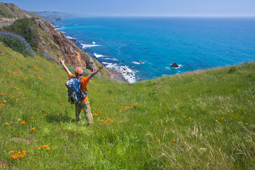 A hiker standing on the green hill  overlooking pacific ocean, Big Sur, California