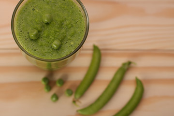  Smoothie with green peas  in a glass and pea pods  on wooden ta