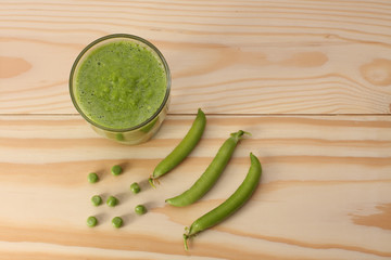  Smoothie with green peas  in a glass and pea pods  on wooden ta