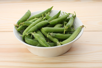 Green  pea pods in white dish  on wooden table