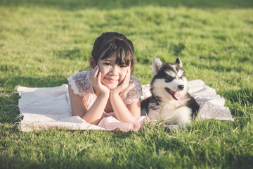 Naklejka na ściany i meble Beautiful asian girl lying on green grass with a siberian husky