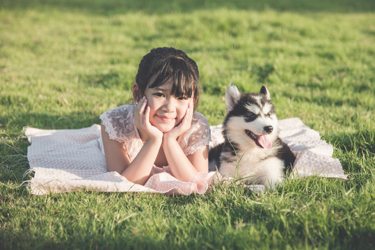 Beautiful asian girl lying on green grass with a siberian husky