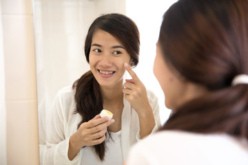 Happy asian woman putting make-up on, smiling at mirror