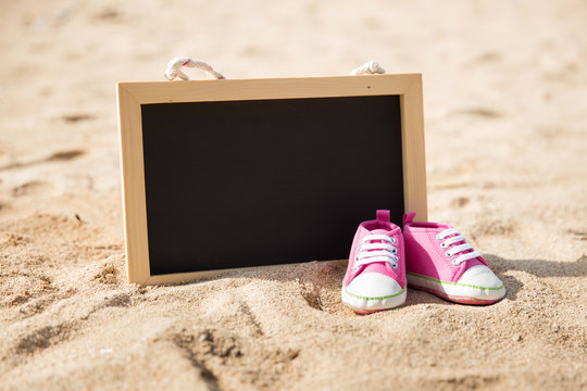 pair of toddler shoes and mini chalk board on the sand