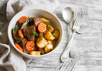 beef goulash with carrots and roasted potatoes in a white bowl on a light wooden background