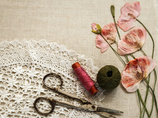 Sewing tools on linen cloth with lace and dry poppies looks like embroidery
