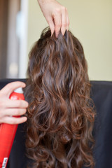 stylist with hair spray making hairdo at salon