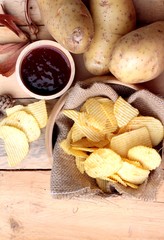 Potato chip and fresh potatoes on wood background