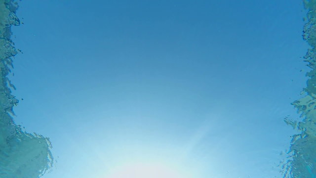SLOW MOTION: Sun and sky through the blue water of swimming pool underwater shot