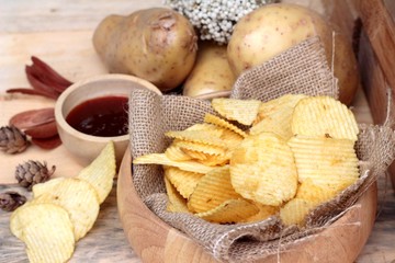 Potato chip and fresh potatoes on wood background