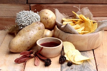 Potato chip and fresh potatoes on wood background