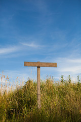 Wooden old road sign pole and blue sky with clouds on background with green grass