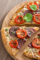 piece of pizza with salami and tomatoes on a wooden board