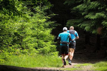 two men running a race on the trail in the green forest