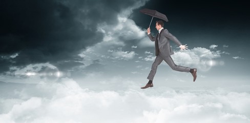 Naklejka premium Composite image of businessman jumping holding an umbrella
