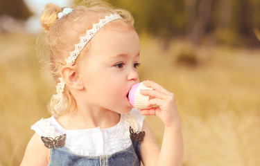 Baby girl 2-3 year old eating cupcake outdoors. Wearing stylish clothes.