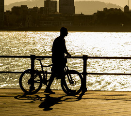 Joven con bicicleta al atardecer caminando por la ciudad