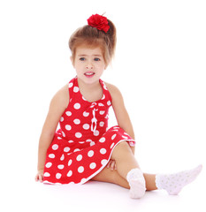 Tender girl in a red polka-dot dress and white socks is sitting 