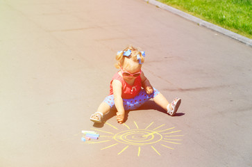 little girl drawing sun with chalks on a street